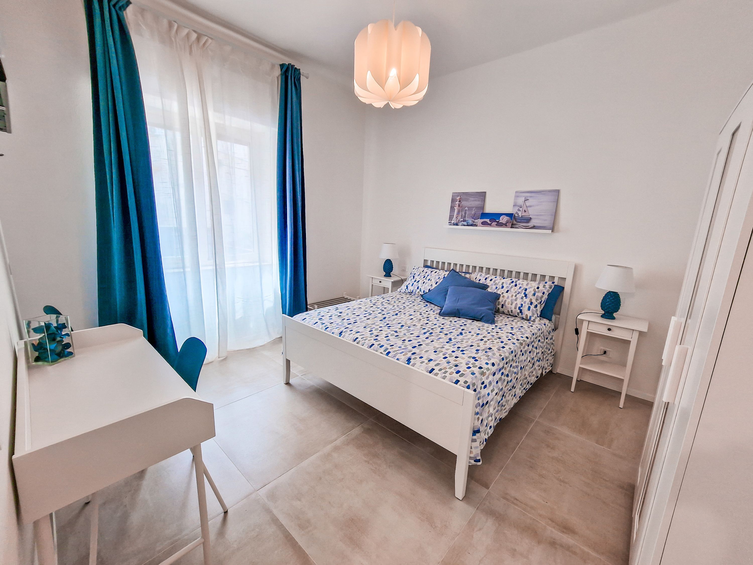 A bedroom with a bed, bedside tables, a desk, and a hanging light fixture.