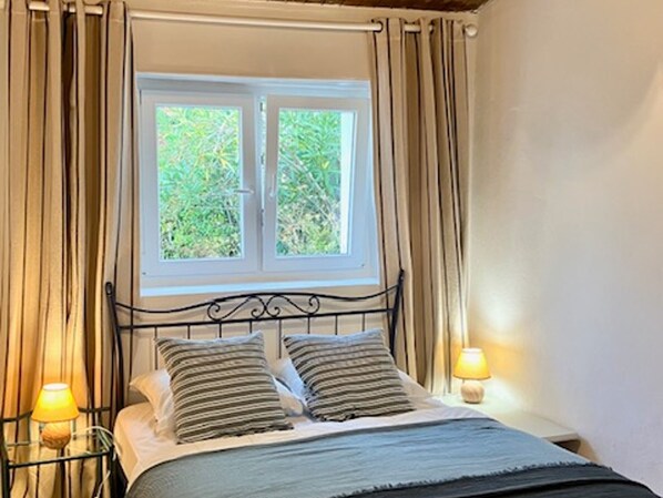 A bedroom with a bed, two bedside lamps, and a window with curtains.