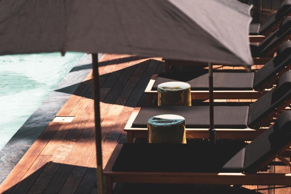 Eine Holzterrasse mit Liegestühlen und einem Tisch mit Blick auf einen Pool.