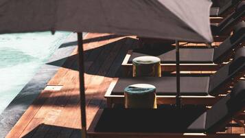 Una terraza de madera con sillones de descanso y una mesa, con vista a una piscina.