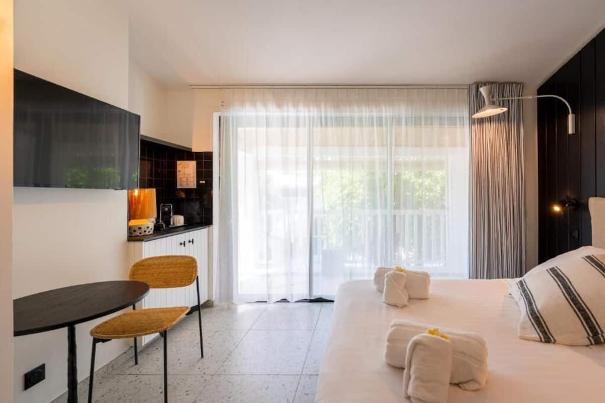 A hotel room with a bed, a desk, a chair, and a large window with curtains.