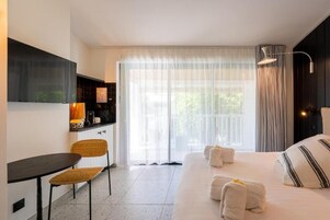 Una habitación de hotel con cama, escritorio, silla y un amplio ventanal con cortinas.