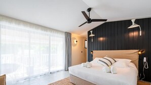 A modern hotel room with a large bed, ceiling fan, and a view of the outdoors through sheer curtains. - Doudou Hotel by Dina Mogarbine (Saint-Paul)