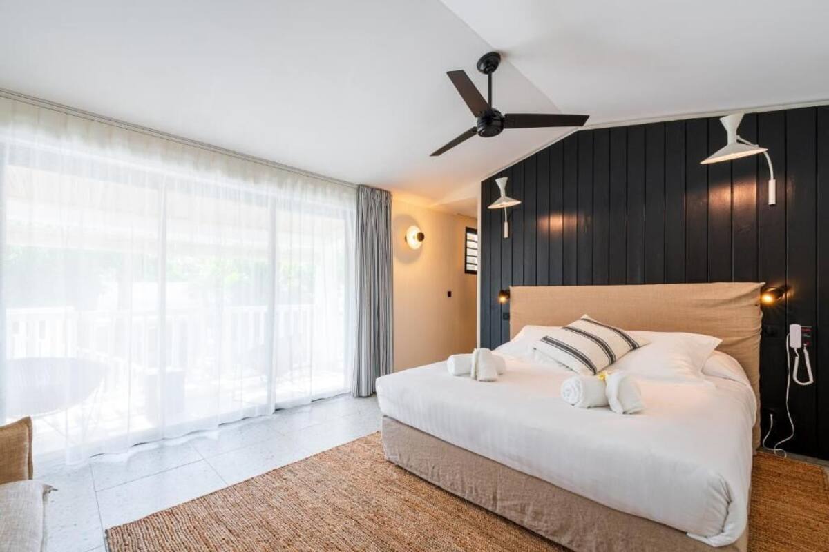 A modern hotel room with a large bed, ceiling fan, and a view of the outdoors through sheer curtains.