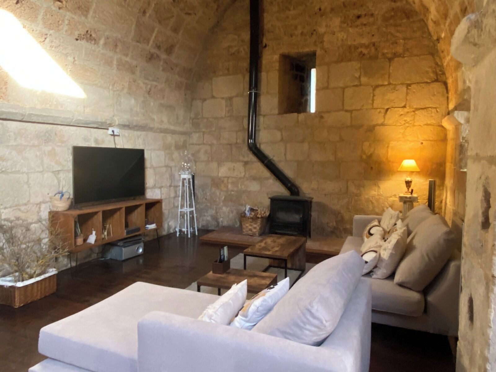 Un salón acogedor con paredes de piedra, un televisor de pantalla plana, un sofá blanco, una mesa de centro de madera y una pequeña chimenea.