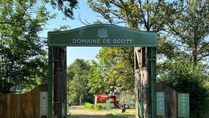 Un arco de madera con el texto "Domaine de Scott" y una máquina expendedora de Coca-Cola en su interior.