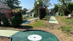 Un campo de mini golf con un césped verde para los hoyos, un círculo blanco en el centro y un camino que lleva al tee.