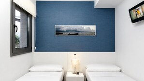 A hotel room with two beds, a nightstand with a lamp, a framed picture on the wall, and a window with a view of the outside.