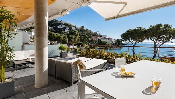 An outdoor patio with a white table, wicker furniture, and a view of the sea and buildings.