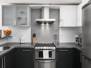 A modern kitchen with stainless steel appliances, a central island, and a grey backsplash. - 2-Bedroom Seafront Apartment in Roses, Pool, WiFi (Roses)