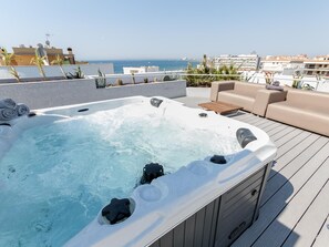 Ein Whirlpool auf einer Terrasse mit Meerblick, eine Sitzecke und ein Holztisch.