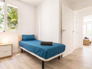 Ein Schlafzimmer mit einem Bett, einem Nachttisch, einem Fenster mit Blick auf Bäume und einer Tür zu einem anderen Raum.