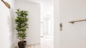 A hallway with a potted bamboo plant, a wooden paddle on the wall, and a door with a handle. - Modern Apartment in Roses - 2 Bedrooms, Near Beach (Roses)