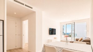 A modern living room with a dining area, a flat-screen TV, and a balcony with a view. - Modern Apartment in Roses - 2 Bedrooms, Near Beach (Roses)