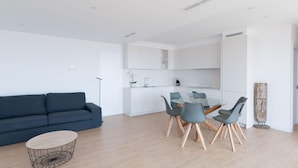 A modern living room with a dark blue sofa, a round coffee table, and a dining area with a glass table and four grey chairs.