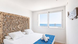A bedroom with a bed, a window with a view, a decorative headboard, and a small table.