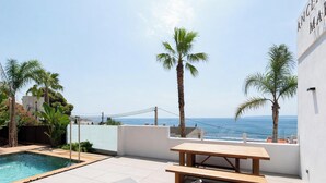 A rooftop pool with a wooden table, palm trees, and a view of the sea. - Modern house with air conditioning and private pool in Roses (Roses)