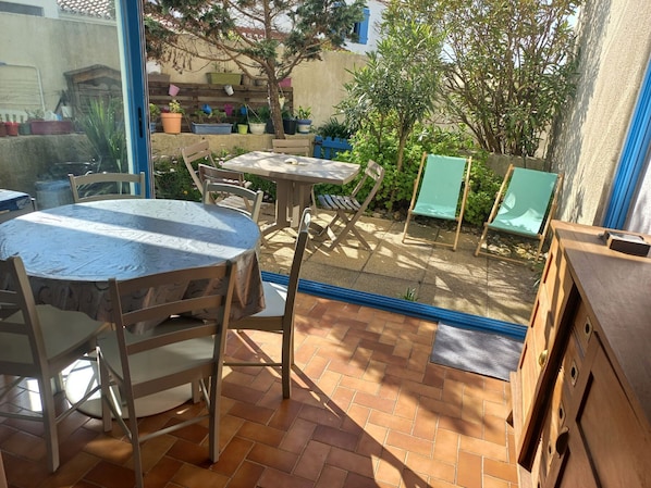 Enjoy a peaceful outdoor space with a round table, chairs, and a bench, surrounded by lush greenery and a glass door leading to the interior.