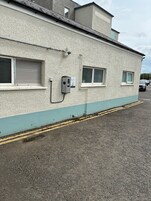 Un edificio con fachada texturizada, dos ventanas con contraventanas y una caja de servicios fijada a la pared.