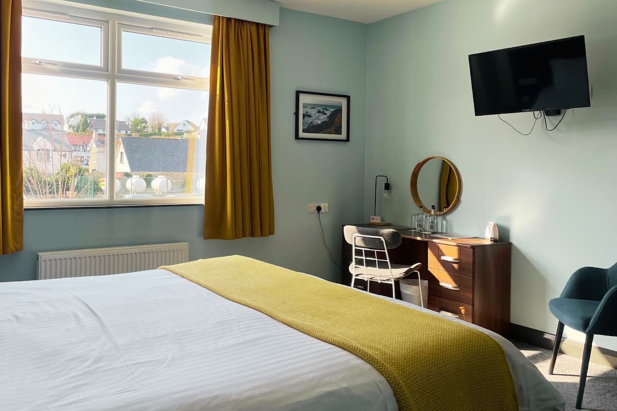 Ein Hotelzimmer mit Bett, Schreibtisch, Stuhl, Fernseher und einem Fenster mit Vorhängen.