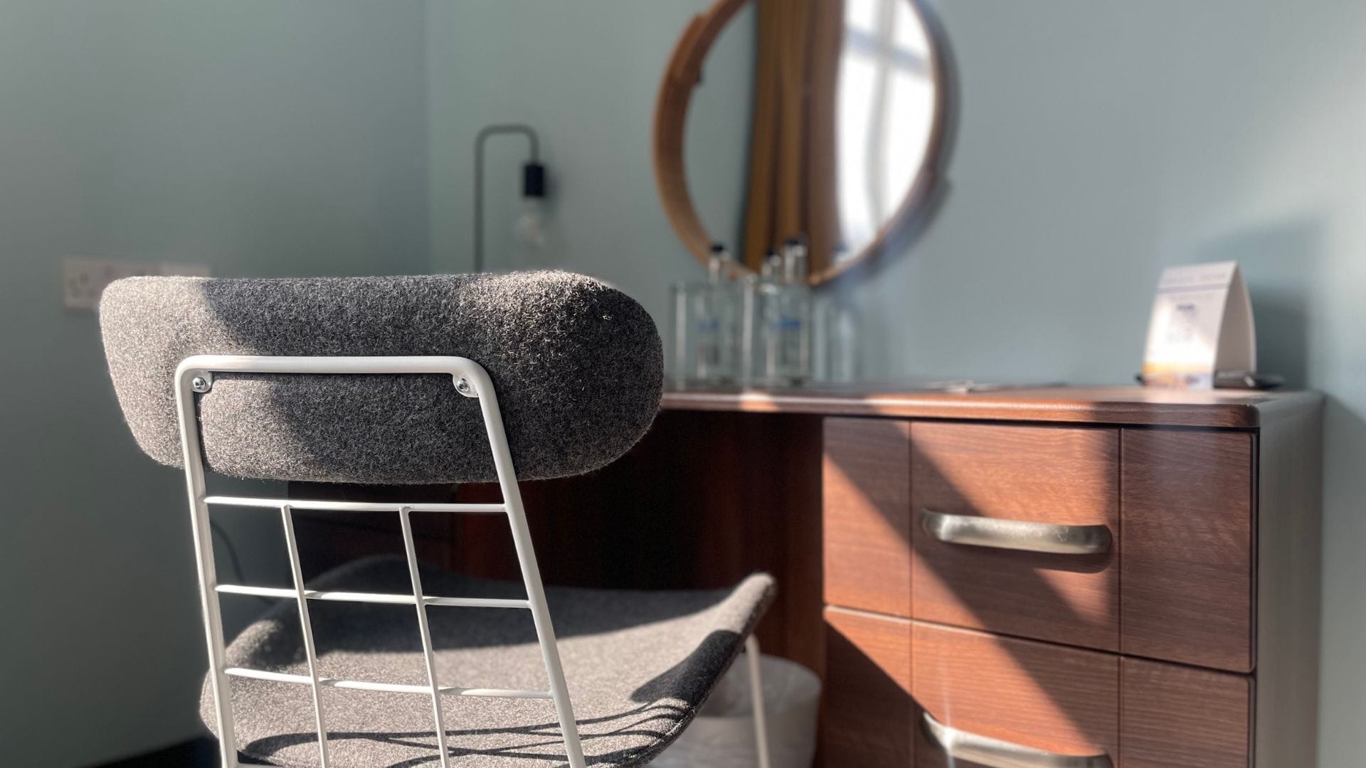 A compact room with a wooden vanity, a mirror, and a chair with a metal frame.