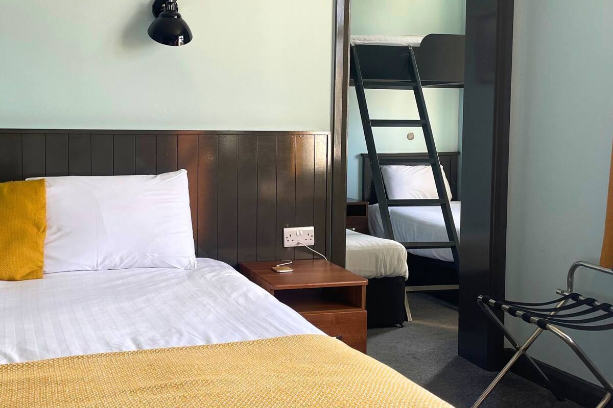 Ein Hotelzimmer mit einem Bett, einem Nachttisch, einem Schreibtisch, einem Sessel und einem Etagenbett.
