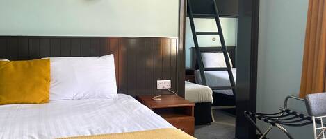 A hotel room with a bed, a nightstand, a desk, a chair, and a bunk bed.