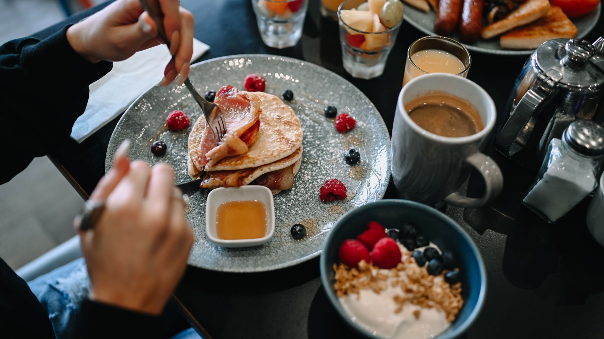 Desayuno con tortitas, frutos rojos, café y salero sobre una mesa.