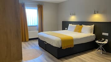Un dormitorio moderno con una cama grande, una mesita de noche con un teléfono y una ventana con cortinas.