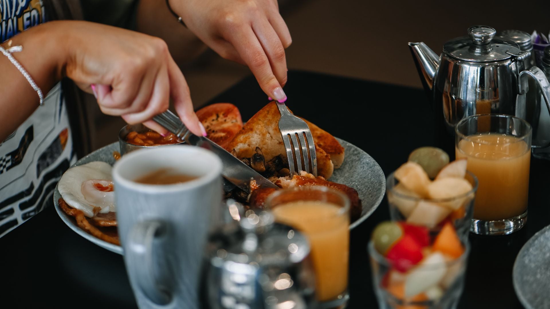 A breakfast setting with a plate of food, a coffee pot, a glass of orange juice, and a fruit bowl.