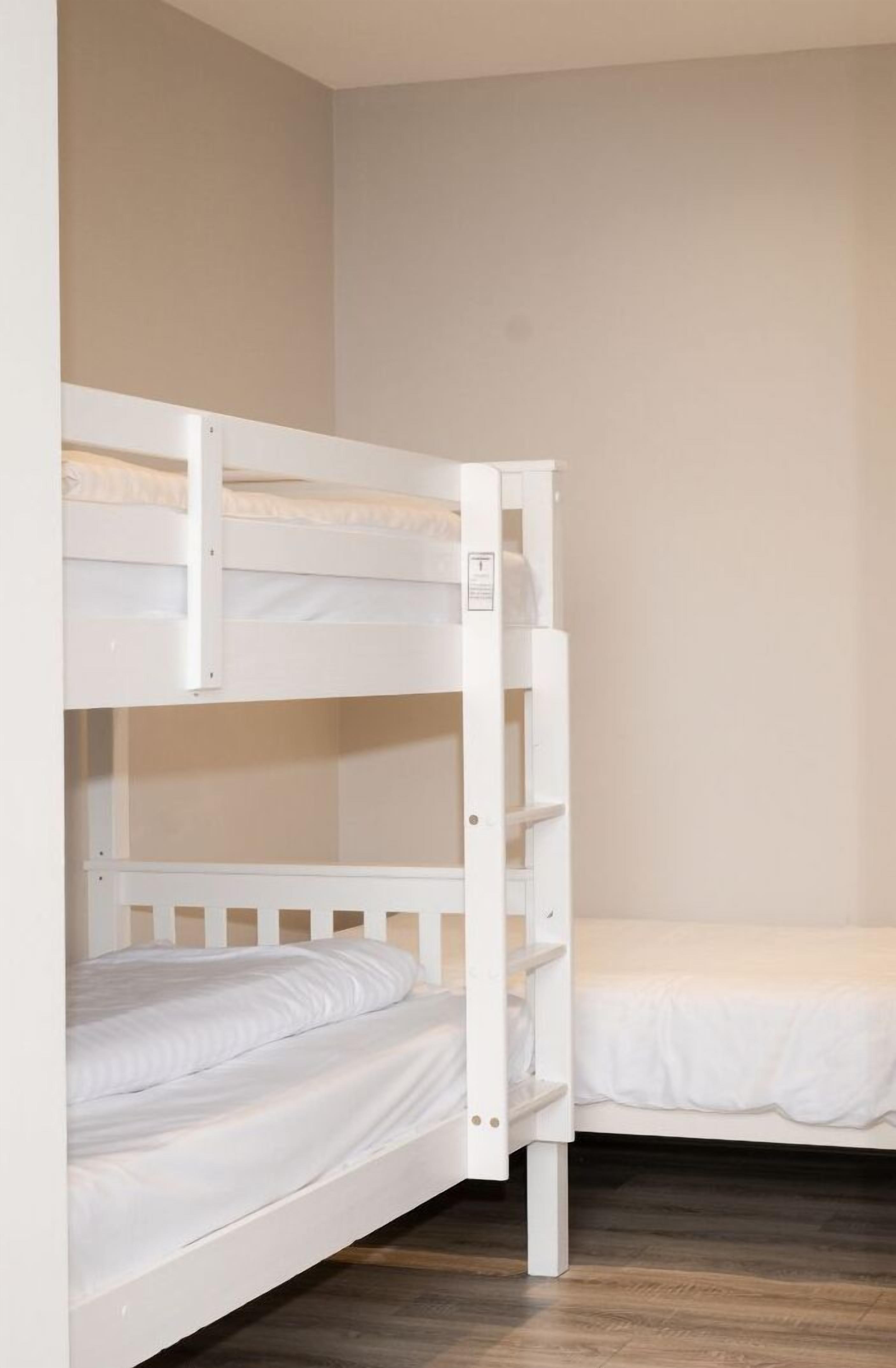 A bunk bed with a ladder, a single bed, and a wooden floor.