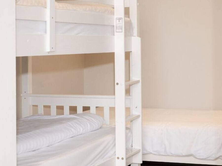 A bunk bed with a ladder, a single bed, and a wooden floor.