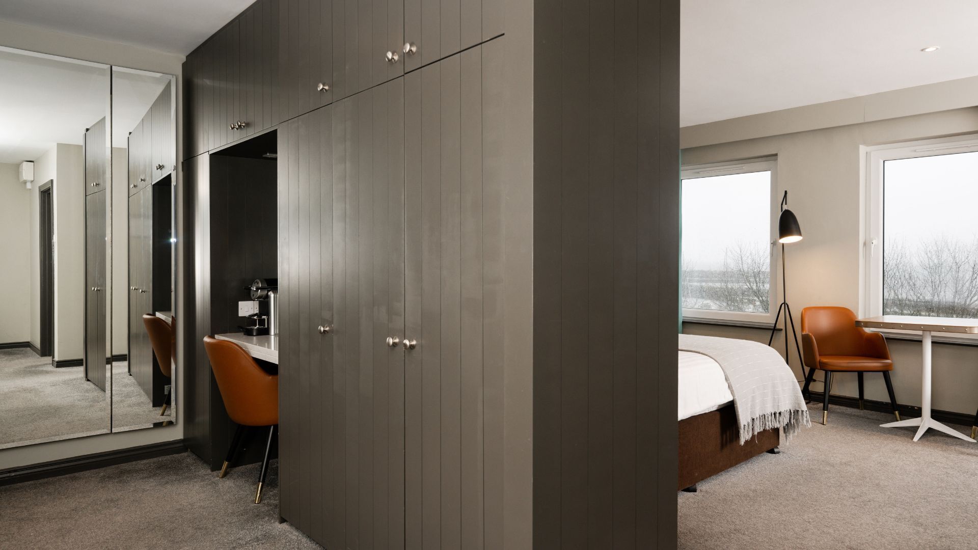 Une chambre dotée d’une grande armoire, d’un bureau, d’une chaise, d’un lit et d’une fenêtre donnant sur un beau paysage.