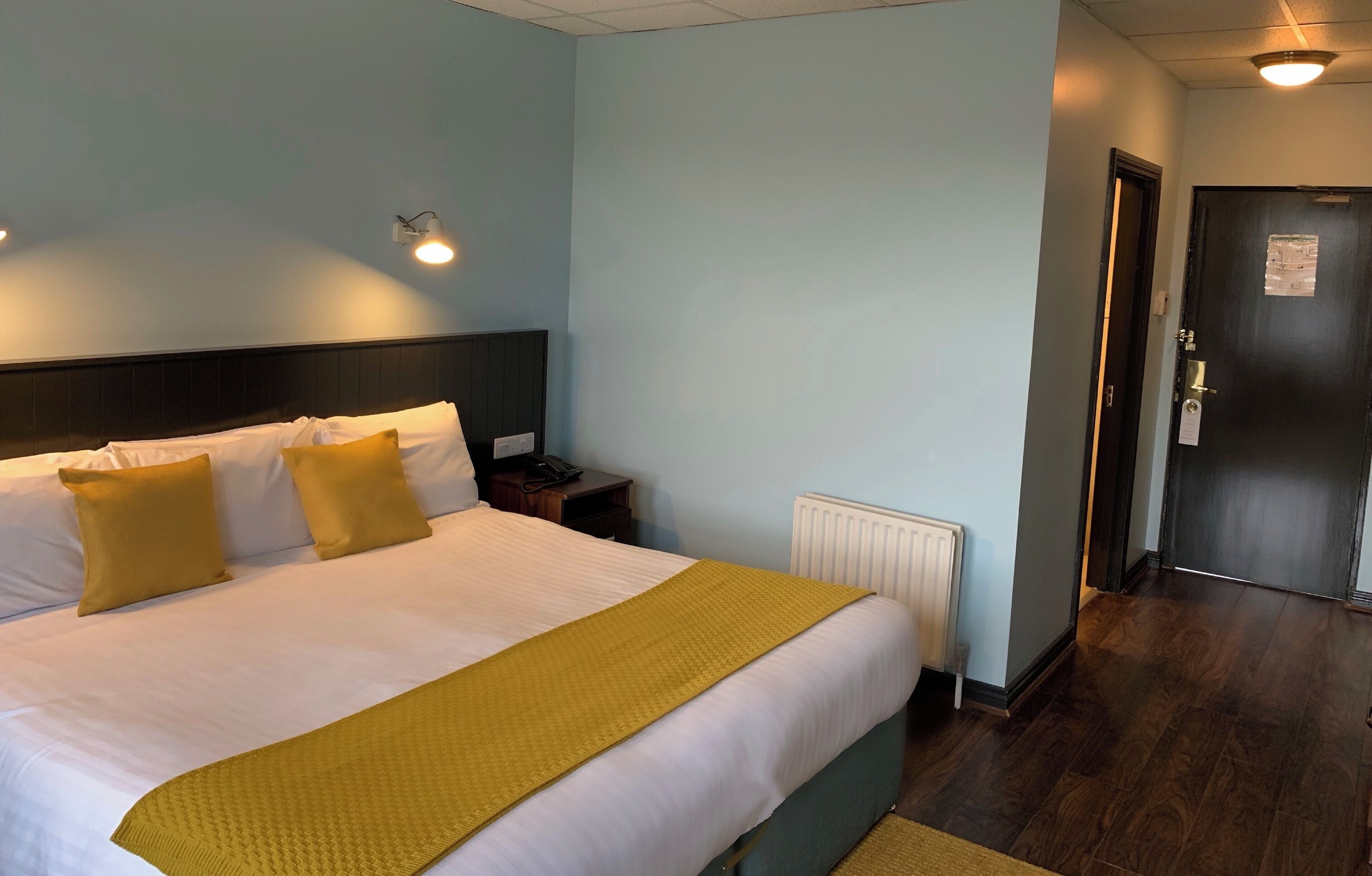 Een hotelkamer met een bed, nachtkastjes, een radiator en een deur.