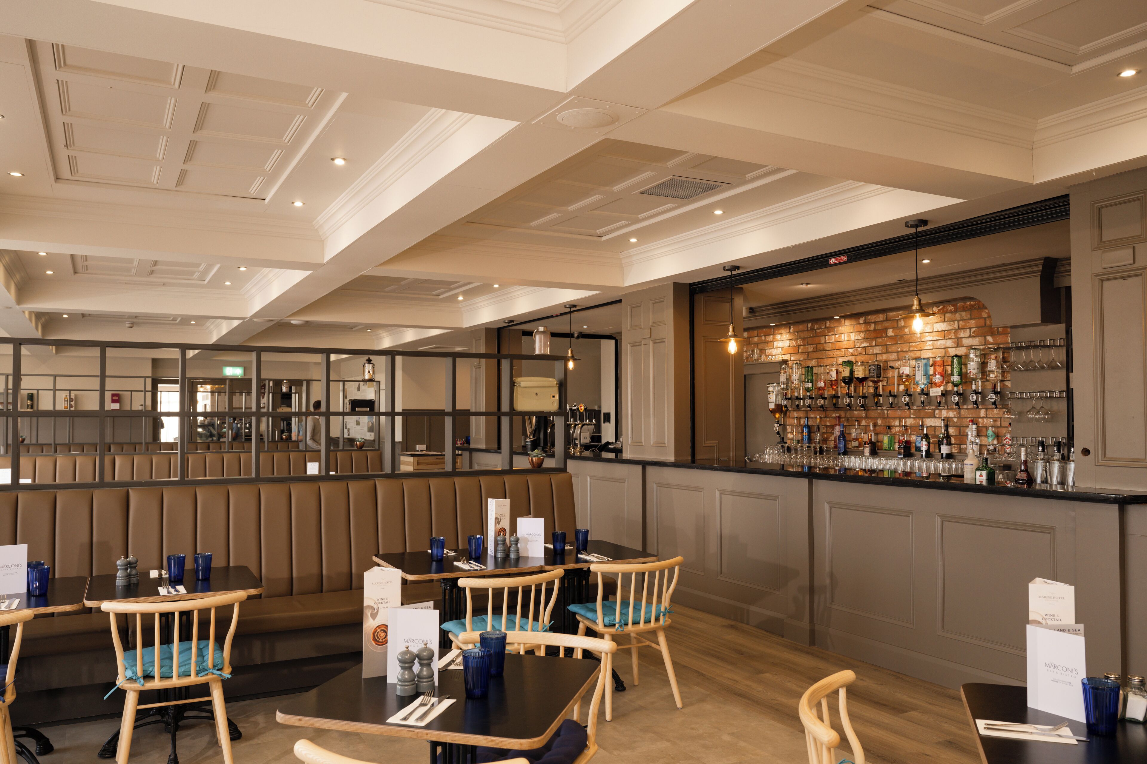 A restaurant with wooden booths and tables, a bar area with a brick wall, and a ceiling with recessed lighting.