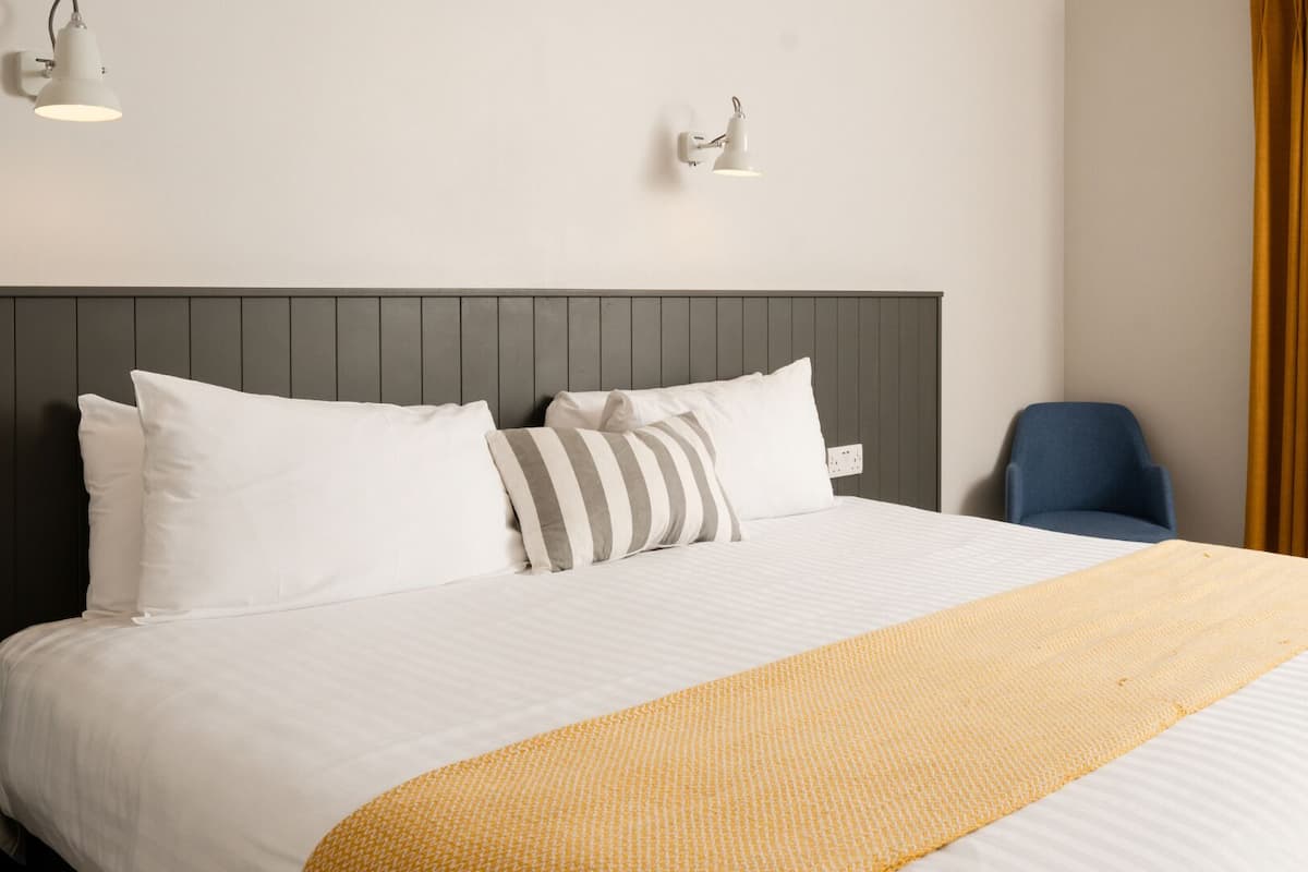 Ein Hotelzimmer mit einem großen Bett, zwei Wandlampen, einem Sessel und einem Fenster mit Vorhängen.