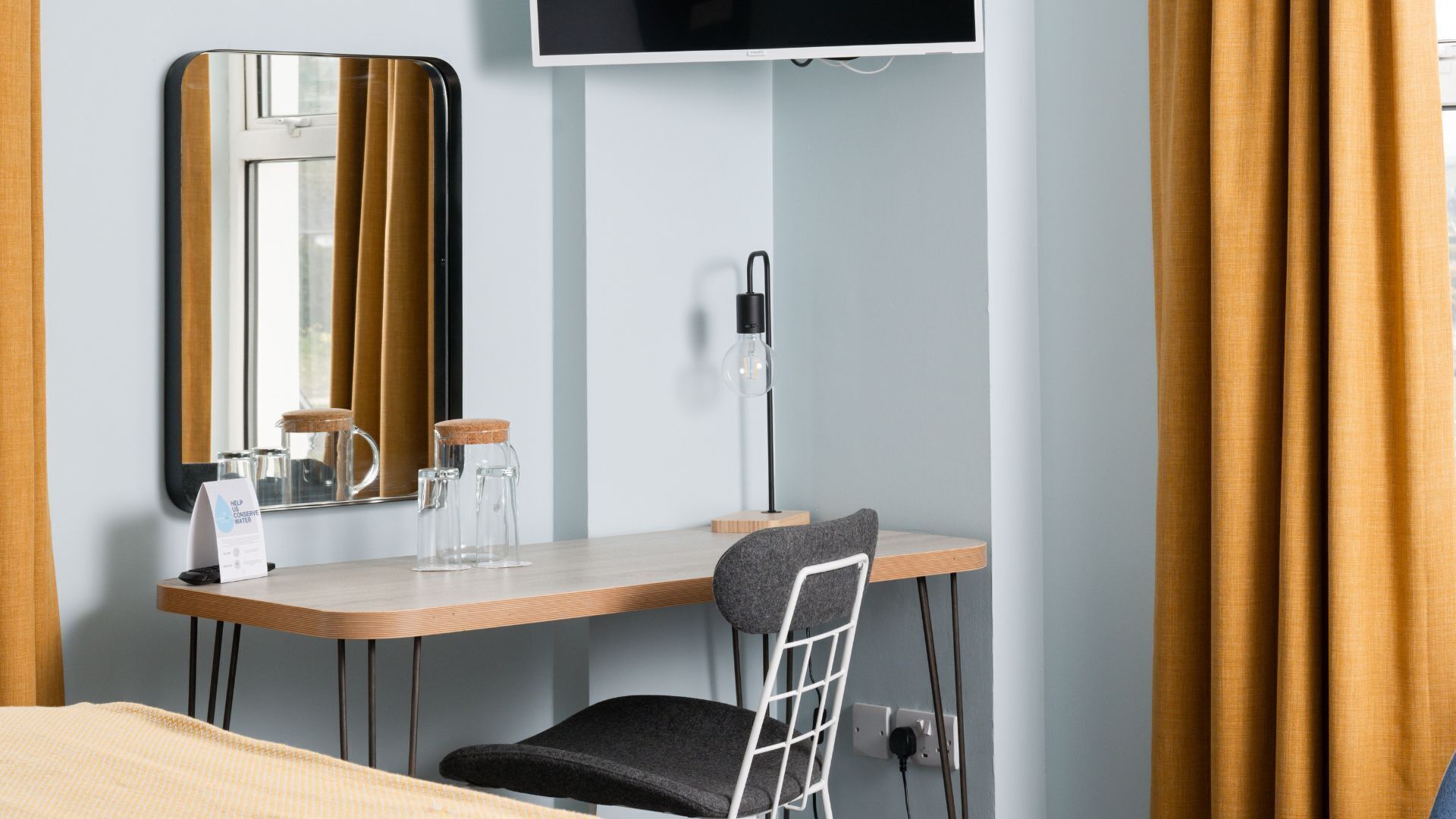 Une chambre d’hôtel avec un bureau en bois, une chaise, un téléviseur fixé au mur et un miroir.