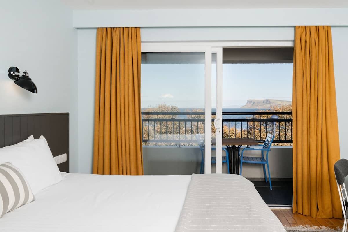 Ein Hotelzimmer mit Bett, Schreibtisch, Stuhl und einem Balkon mit Vorhängen.