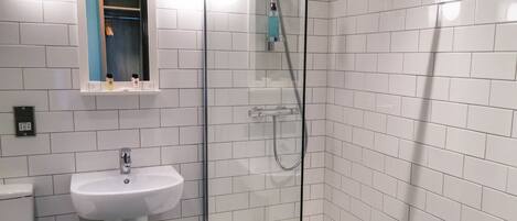 Un baño con paredes de azulejos blancos, un lavamanos blanco y una zona de ducha con mampara de vidrio.