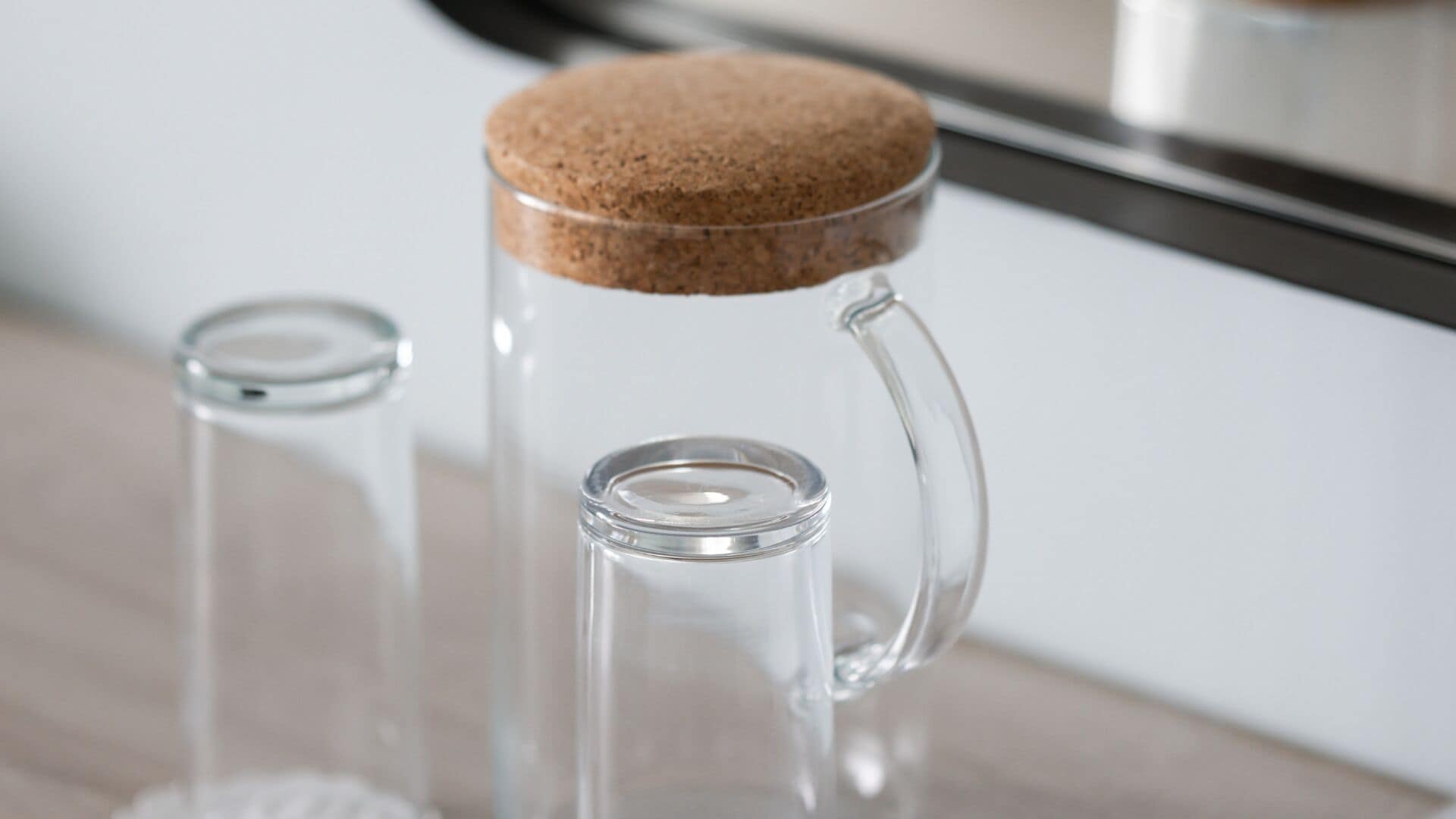 A clear glass mug with a cork stopper and a clear glass container with a cork lid.