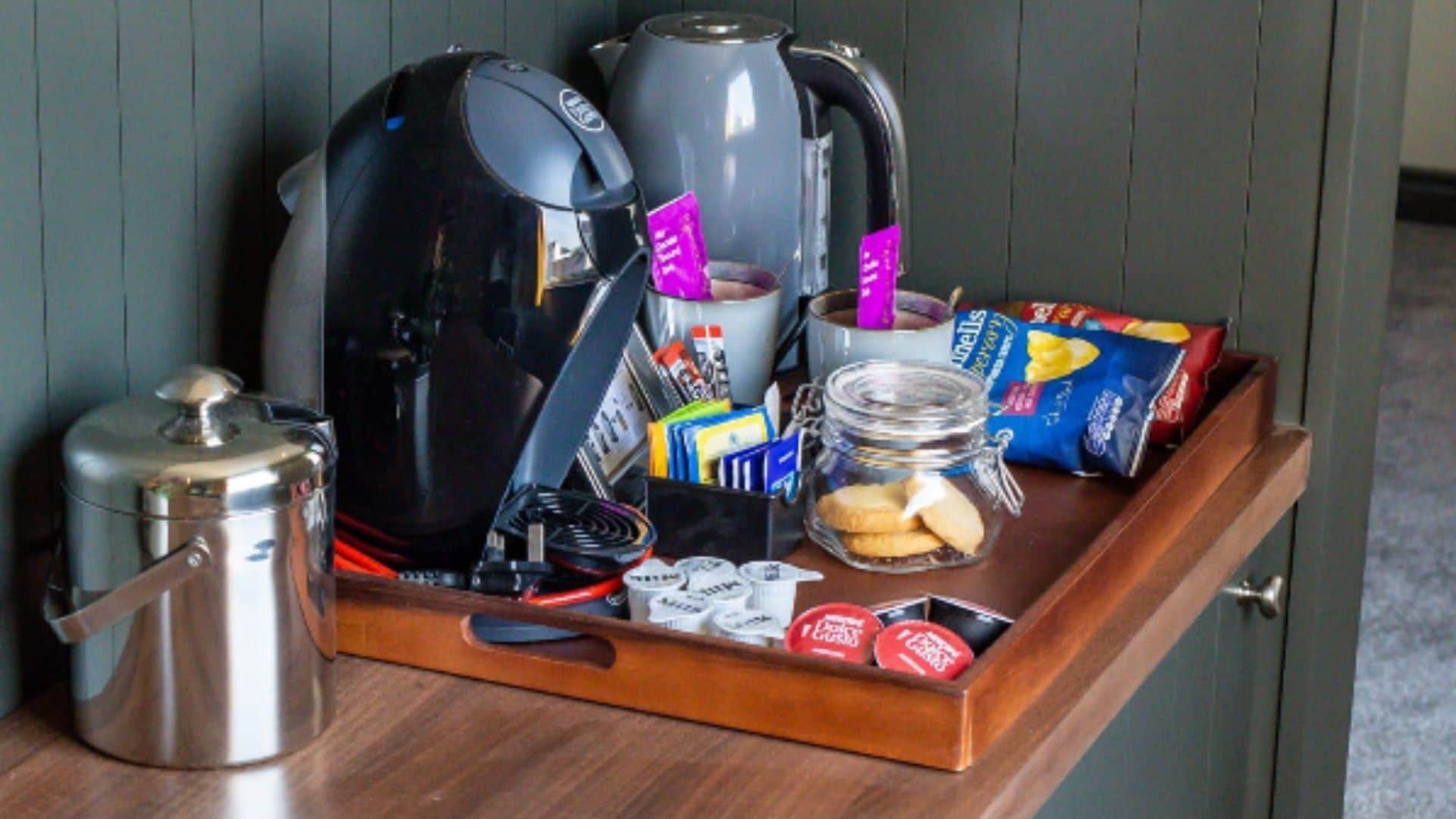 Ein Tablett mit einer Kaffeemaschine, einem Thermos, Snacks und einem Glas Kekse.