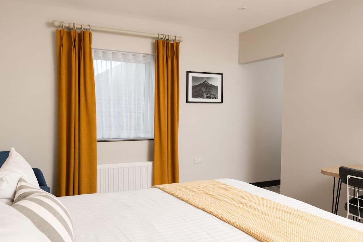 Ein Hotelzimmer mit Bett, einem Fenster mit Vorhängen, einem Wandbild und einer Nachttischlampe.