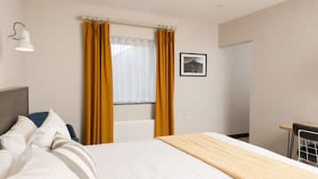 Una habitación de hotel con cama, ventana con cortinas, un cuadro en la pared y una lámpara de noche.