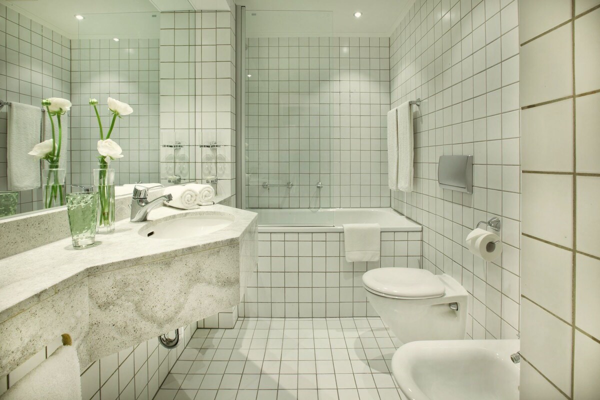A modern bathroom with a large mirror, a sink, a bathtub, and a toilet.