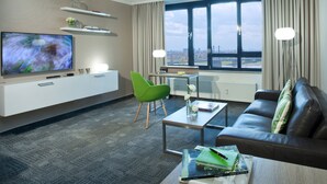 Un salon moderne avec un téléviseur à écran plat, un fauteuil vert, un canapé en cuir et une table basse.