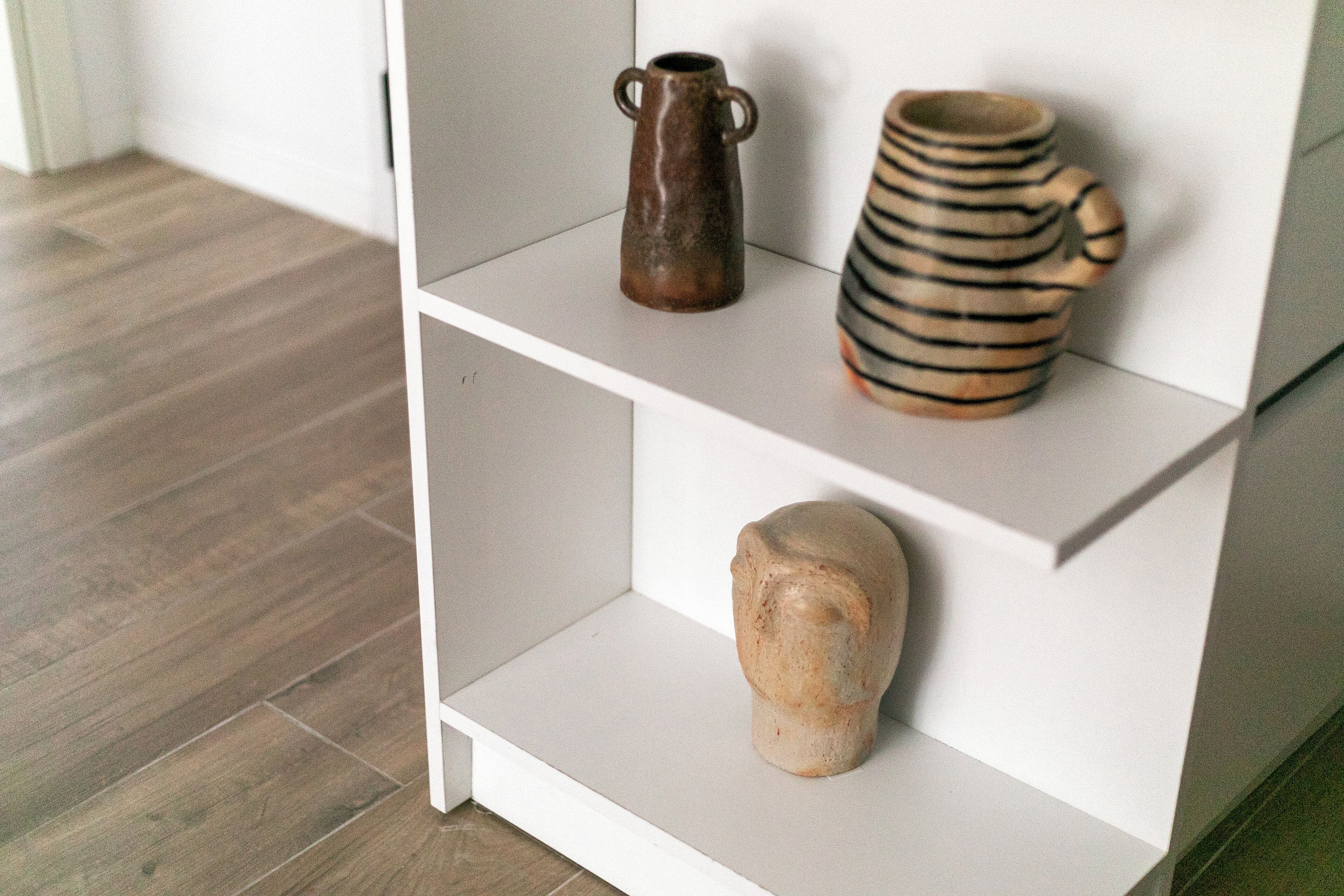 Un mobiletto contenitore bianco con tre vasi in ceramica esposti.