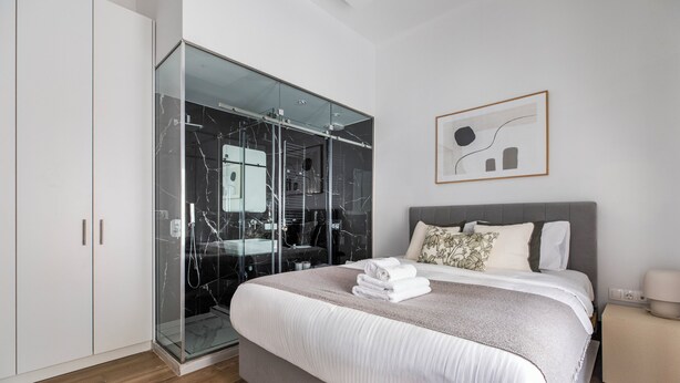 Un dormitorio moderno con una cama grande, un vestidor y un box de ducha de vidrio.