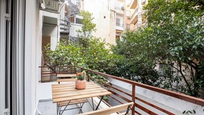 Un balcón con una mesa de madera, una planta en maceta y una barandilla de metal.