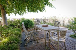 An outdoor patio with a table and chairs, surrounded by greenery and a view of a fence. - Hestar Husid, a designer home with a garden near Amsterdam (Weesp)