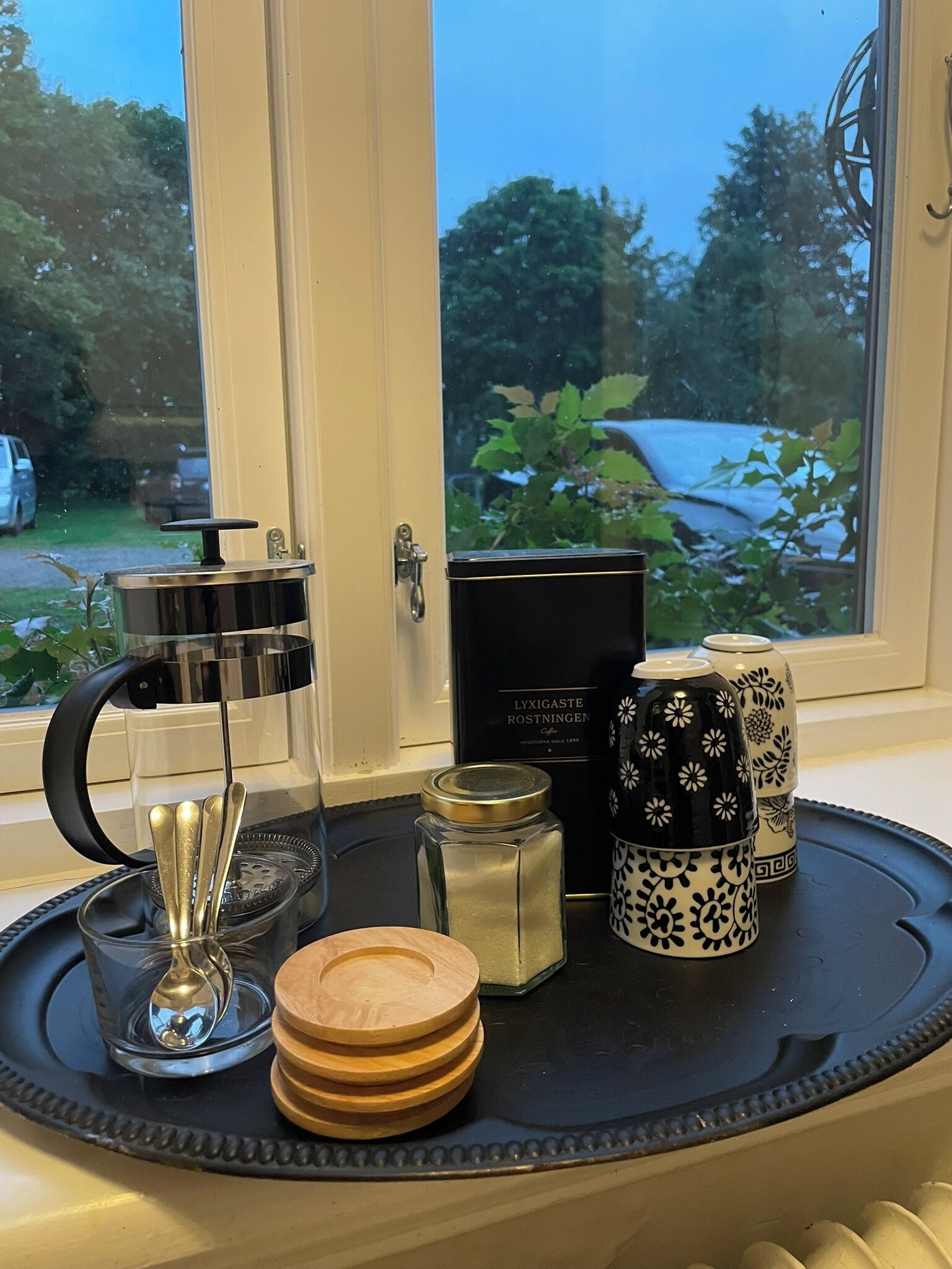 Un plateau contenant une machine à café, un bocal en verre, une boîte et des objets décoratifs, le tout posé sur un rebord de fenêtre.
